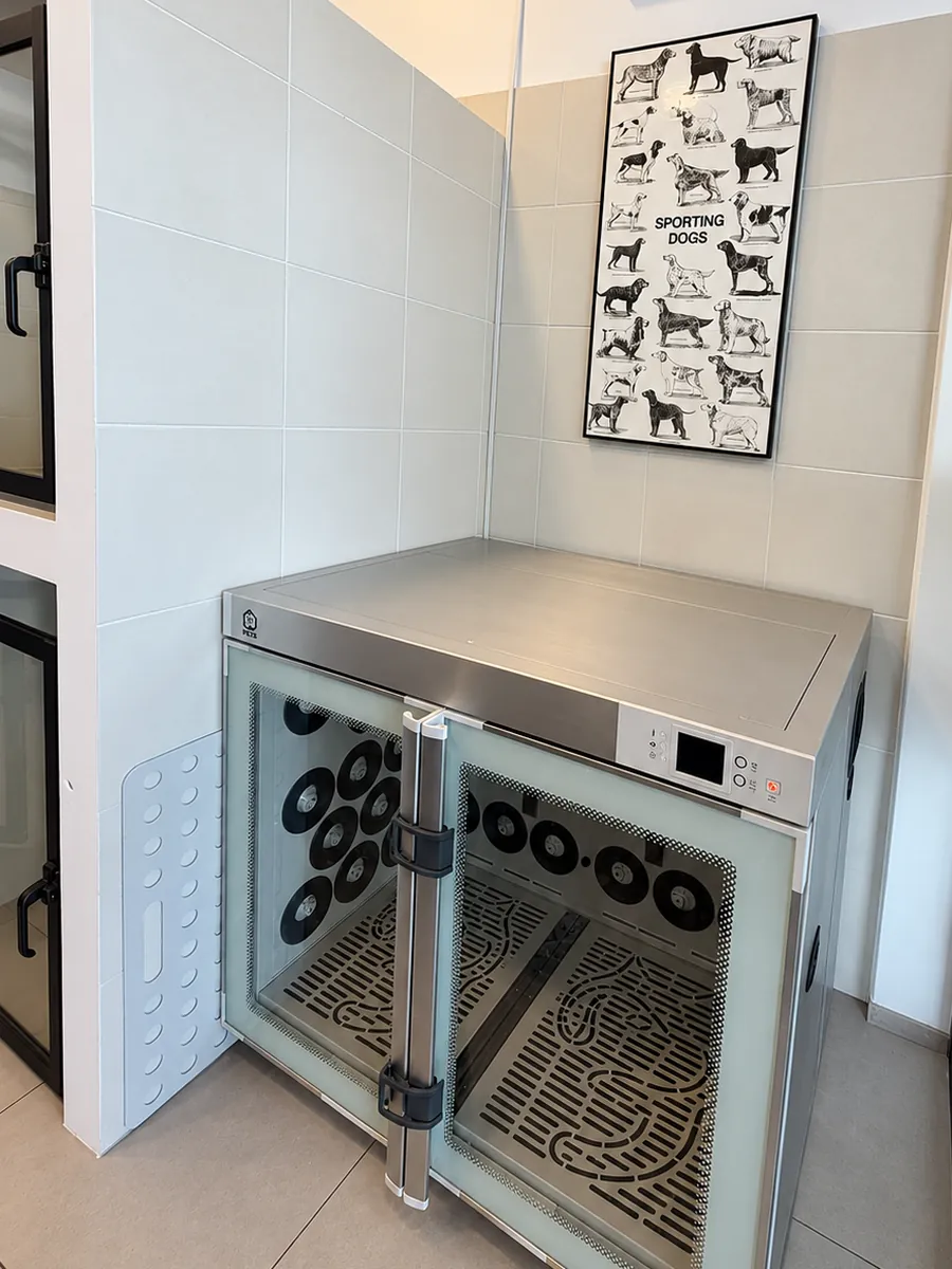 Cabina de secado de acero inoxidable en la peluquería, junto a las jaulas y bajo un cuadro de razas de perros